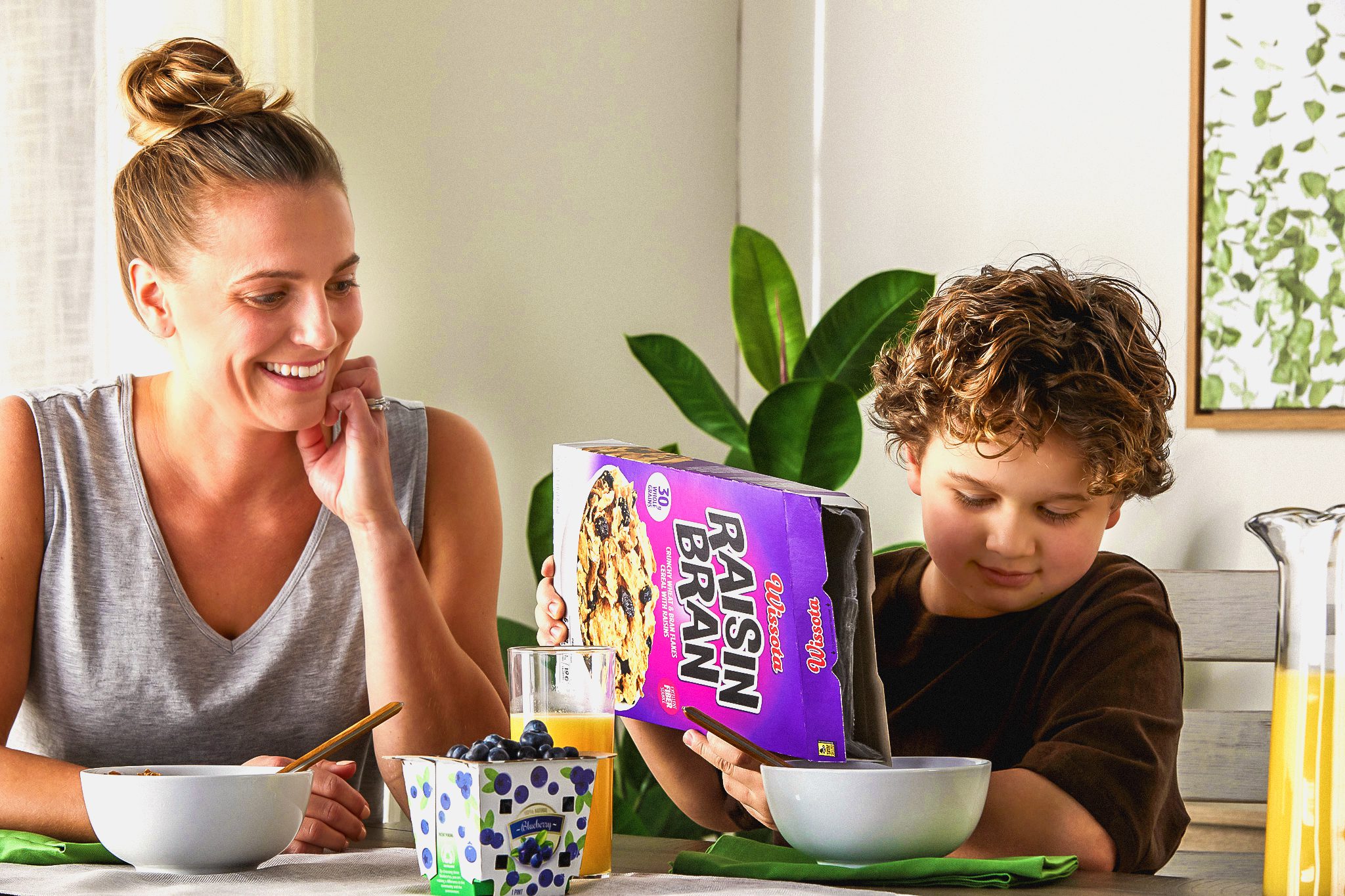 Madre observando a su hijo verter una caja de cereales en un tazón