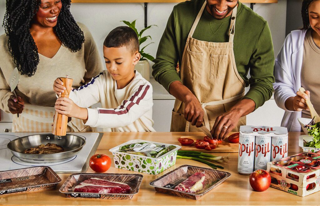 Cuatro miembros de una familia cocinan y usan varios productos de Graphic Packaging, incluida la bandeja PaperSeal, ProducePack y más.