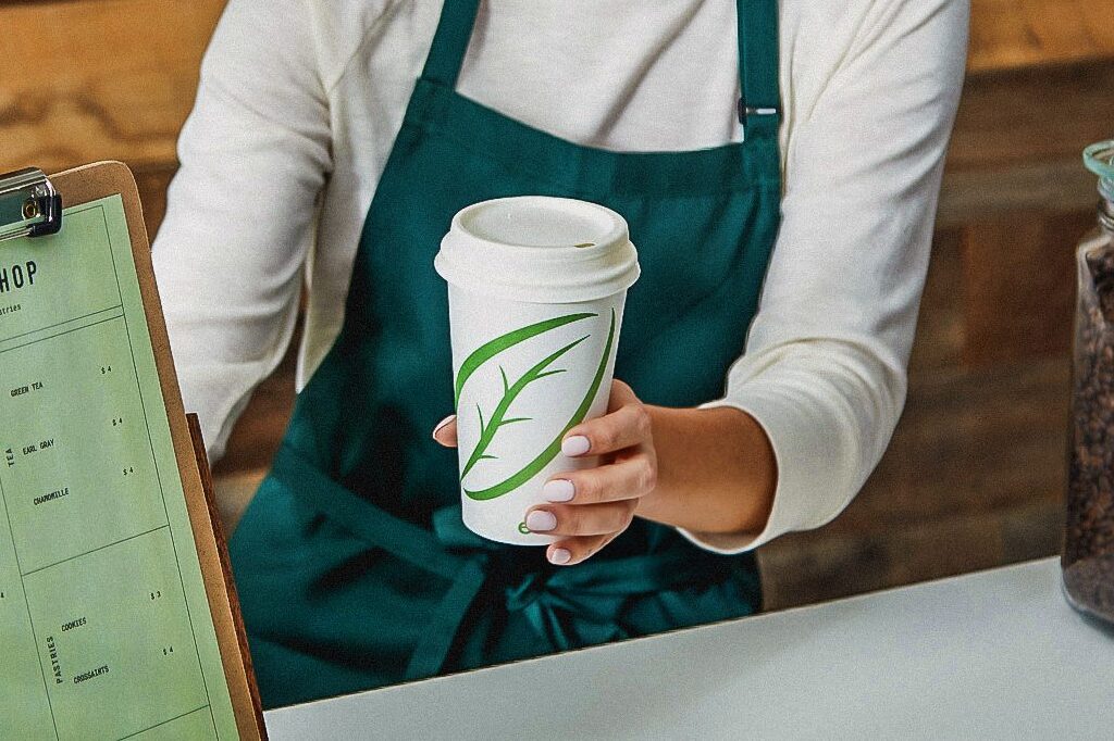 Un barista entrega café a alguien usando el vaso para bebidas calientes ecotainer de Graphic Packaging